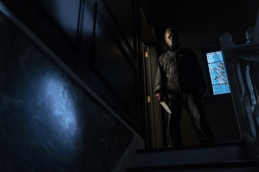 Michael Myers (Courtney) standing at the top of his stairs in his childhood home, looking down at Allyson (Matichak).