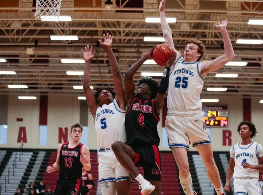 Westside’s CJ Mitchell drives in for the layup against Millard North’s Nick Dolezal and David Harmon. - Photo by Zoe Gillespie